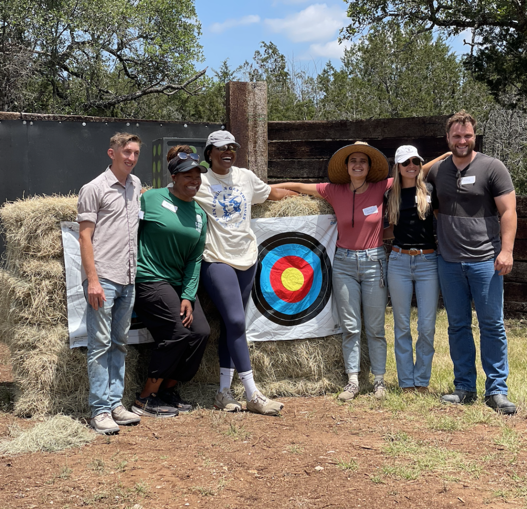 Corporate group smiling in front of an archery target displaying the value of nature based team building activities at Horse + Bow in Austin, TX