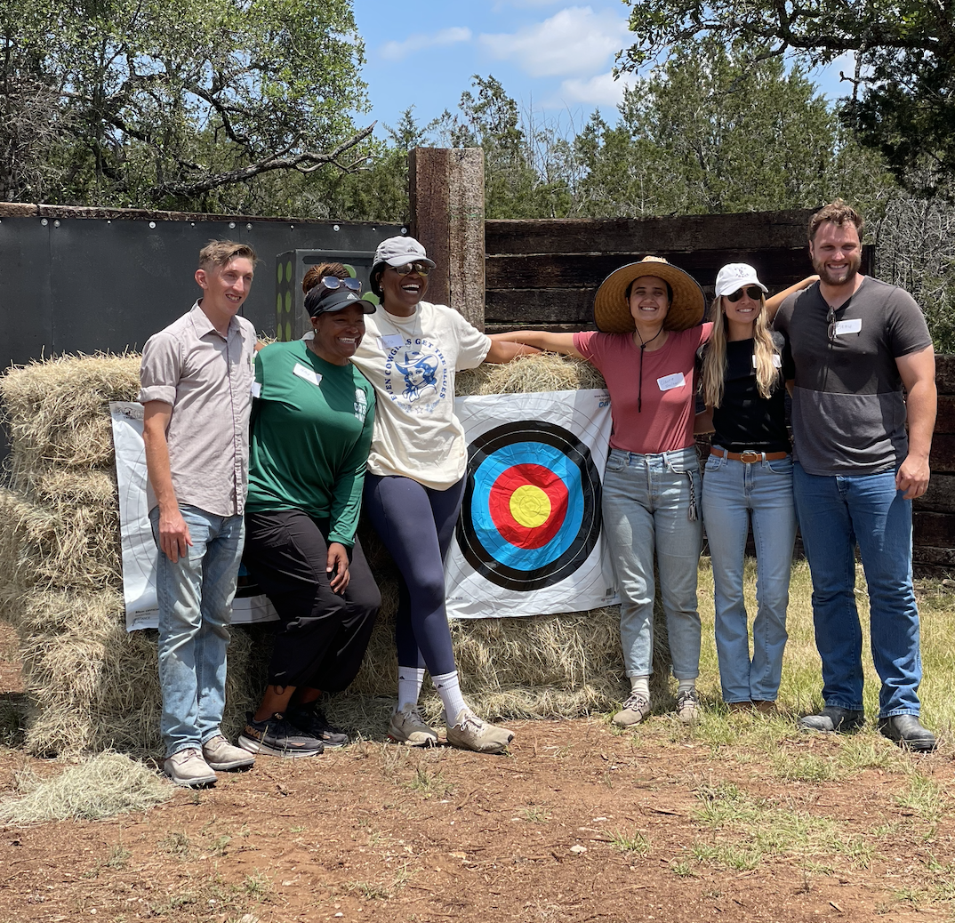 Corporate group smiling in front of an archery target displaying the value of nature based team building activities at Horse + Bow in Austin, TX